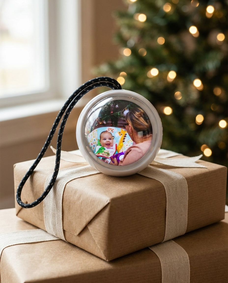A Glowkeep memory orb on a stack of kraft-wrapped gifts under the tree, a baby's photo on the screen