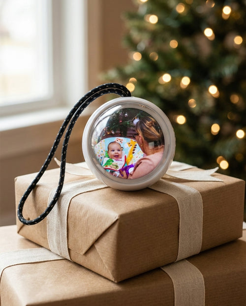 A Glowkeep memory orb on a stack of kraft-wrapped gifts under the tree, a baby's photo on the screen
